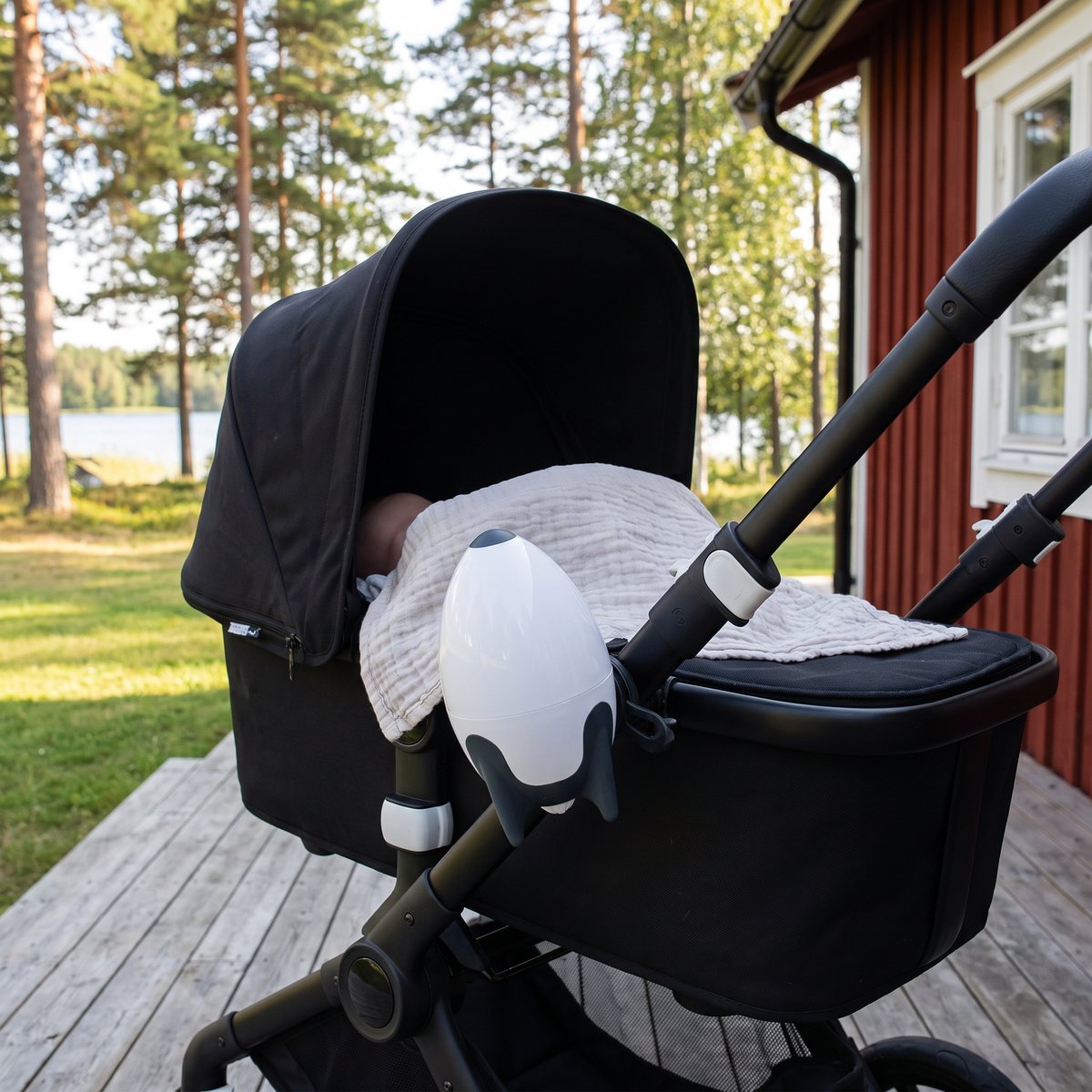 Vit raketformad Rockit Rechargeable monterad lodrätt på sidan av handtaget till en svart barnvagn på en altan vid en röd stuga och en sjö