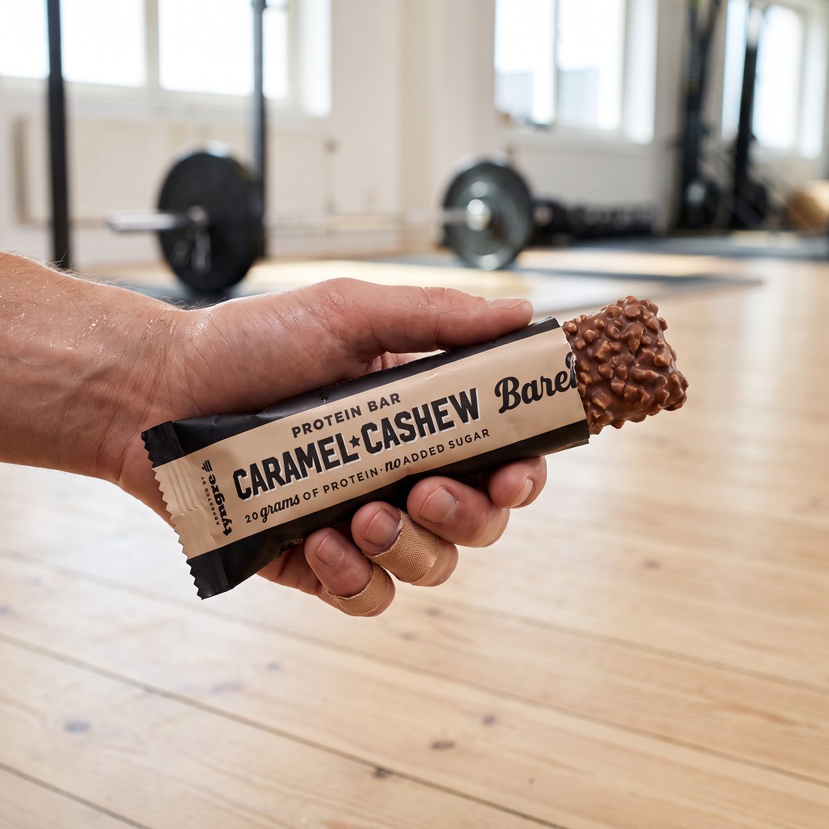 Proteinbar med karamell och cashew hålls i handen i ett ljust svenskt gym med trägolv