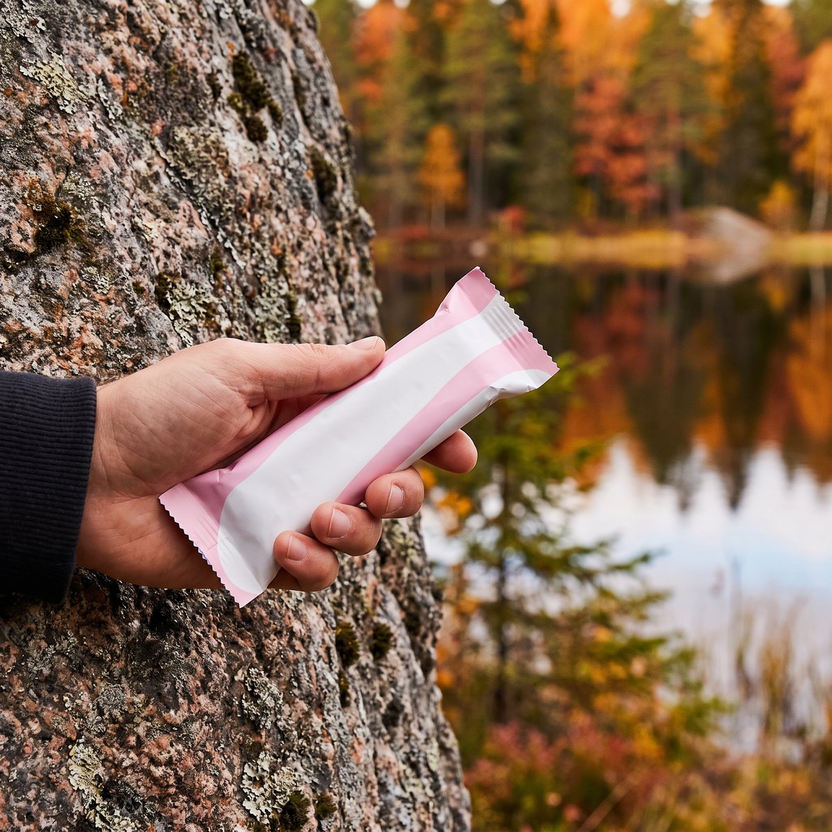 Proteinbar med jordnöt hålls i handen vid en skogssjö i svensk höstnatur