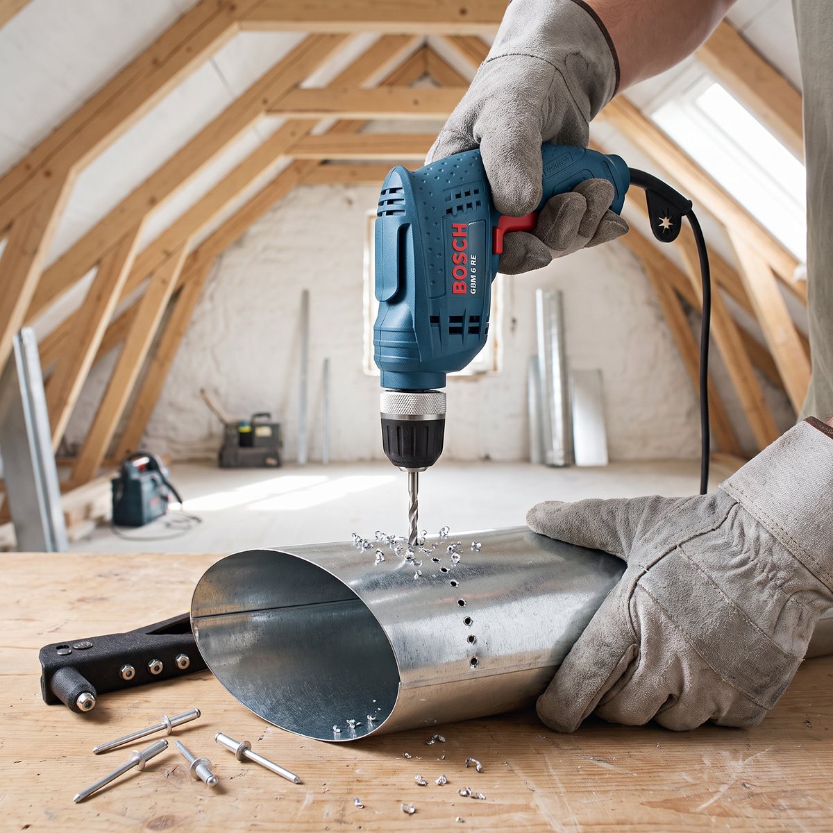 Bosch GBM 6 RE som borrar små nithål i en ventilationskanal av plåt på en arbetsbänk på en svensk vind