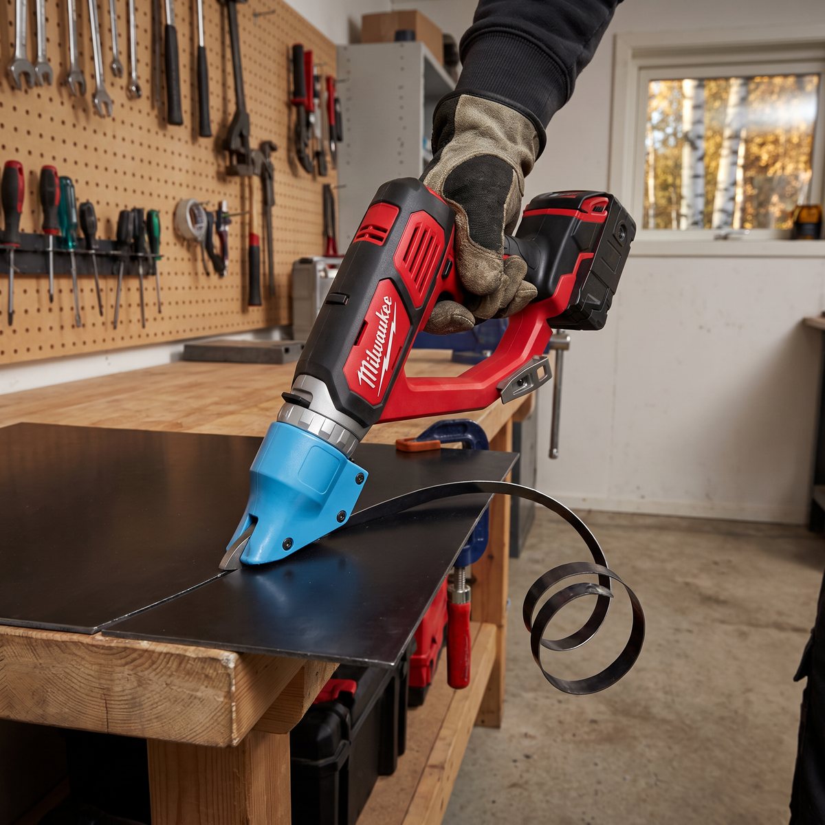 Milwaukee M18 BMS20 klipper en tjock svart stålplåt på en arbetsbänk i ett garage med verktygstavla