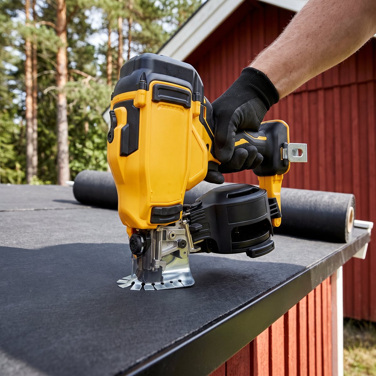 Gul och svart batteridriven rullspikare från Dewalt mot takpapp på ett förrådstak, rött trähus och tallar i bakgrunden