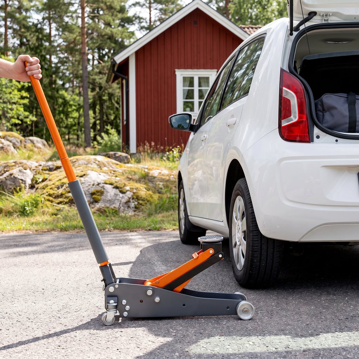 Grå och orange Bahco BH1A1500 aluminiumdomkraft under en vit småbil vid en röd sommarstuga med tallar och granithällar