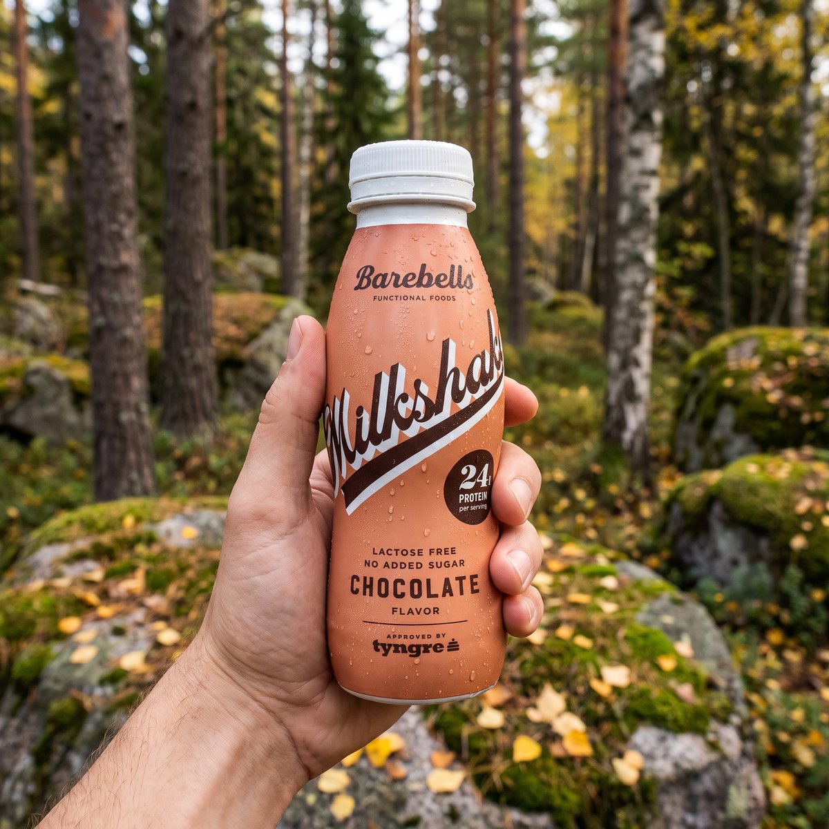 Barebells Milkshake Chocolate i handen efter en löprunda i en svensk höstskog med tall, björk och mossiga stenar