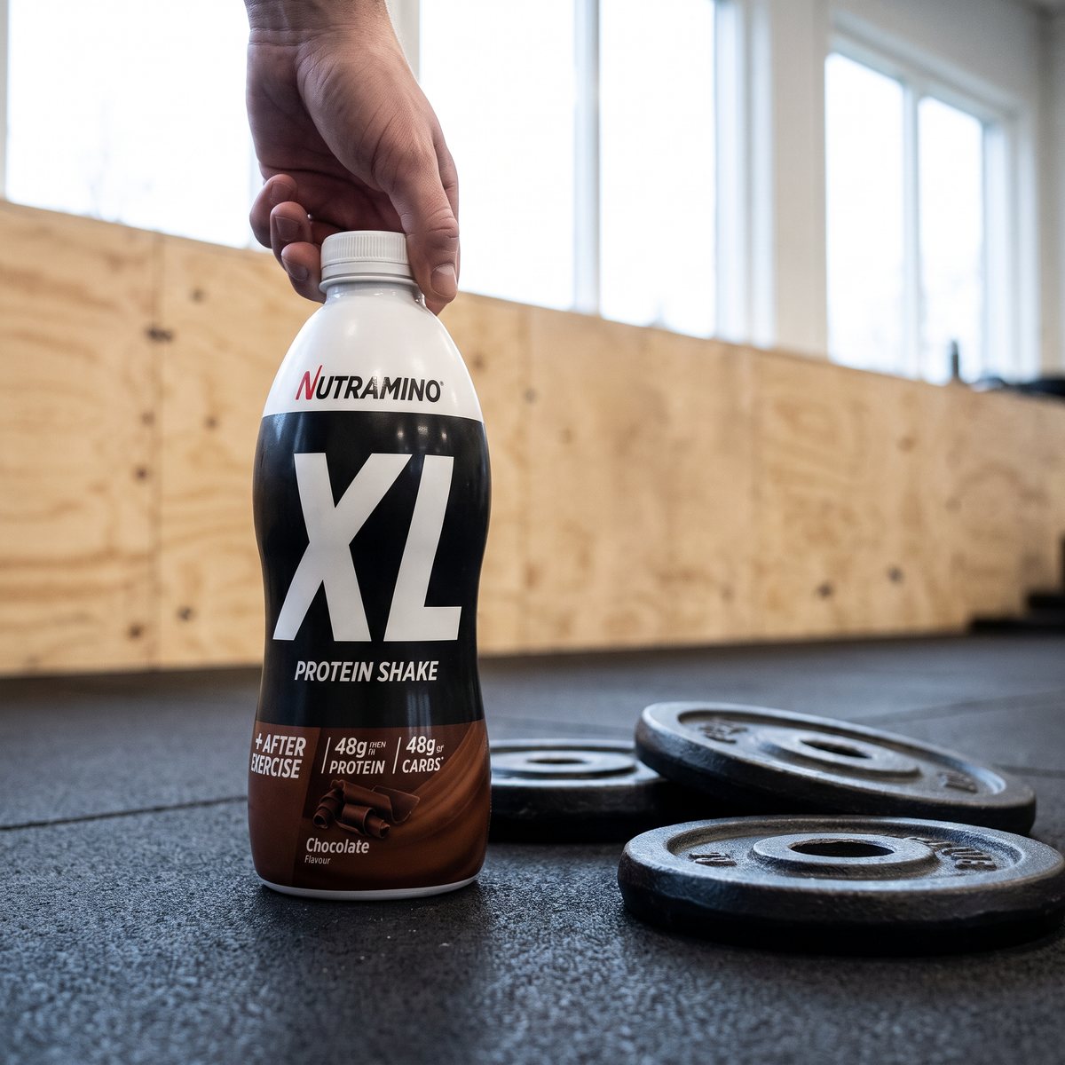 Nutramino XL Protein Shake Chocolate på gummigolvet i ett gym bredvid viktskivor