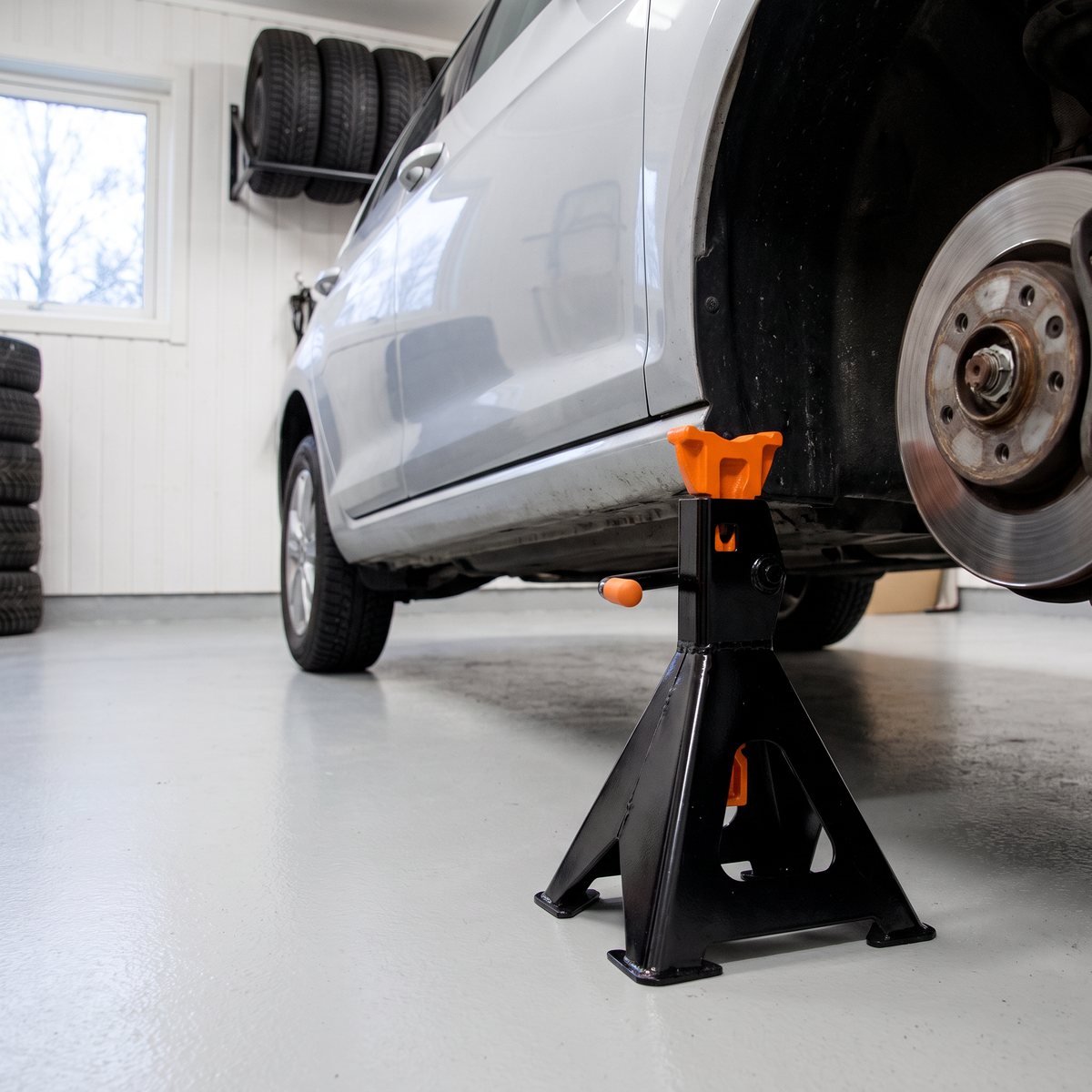 Svart pallbock med orange sadel under tröskeln på en silverfärgad halvkombi med framhjulet avtaget i ett vitt svenskt garage