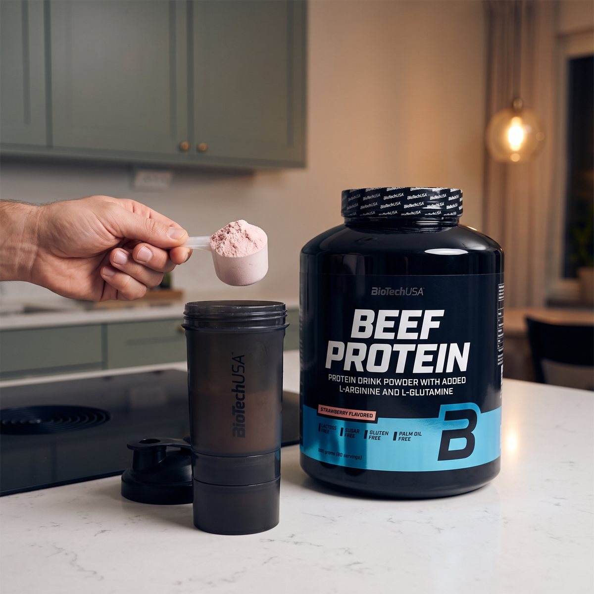 BioTechUSA Beef Protein-burken på en vit stenbänk där en skopa rosa jordgubbspulver hålls över en shaker, i ett svenskt kök med induktionshäll