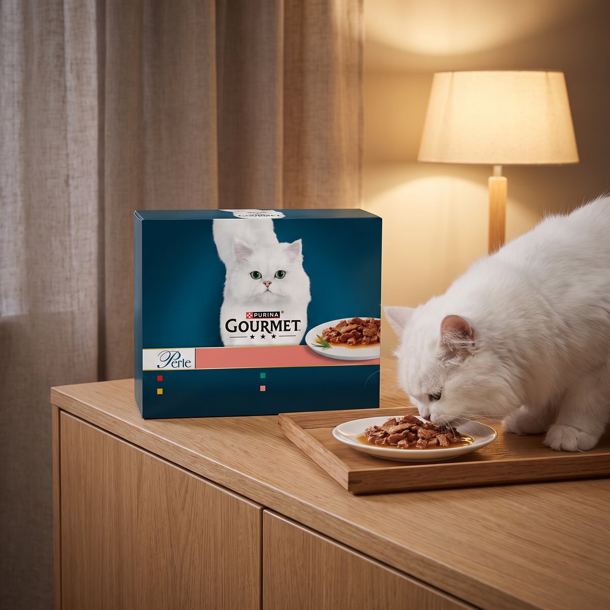 En vit långhårig katt äter små filébitar i sås från ett porslinsfat bredvid en Gourmet Perle-låda på en ekskänk i ett svenskt vardagsrum i lampsken
