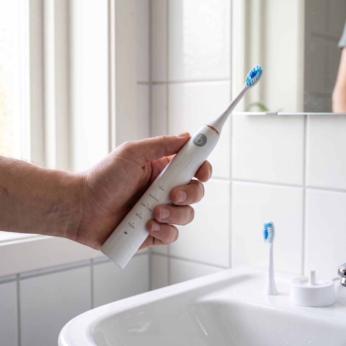 Hand håller vit Beconfident Sonic Whitening eltandborste i ett svenskt badrum