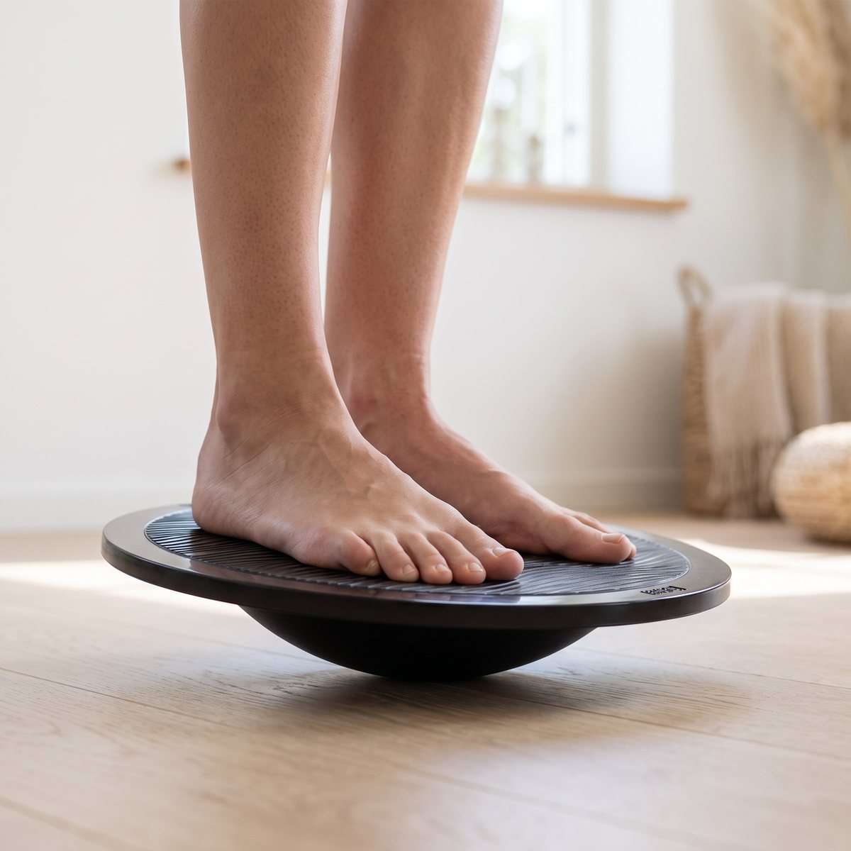 Casall Balance Board II, en svart rund balansbräda, med bara fötter i ett ljust svenskt vardagsrum.