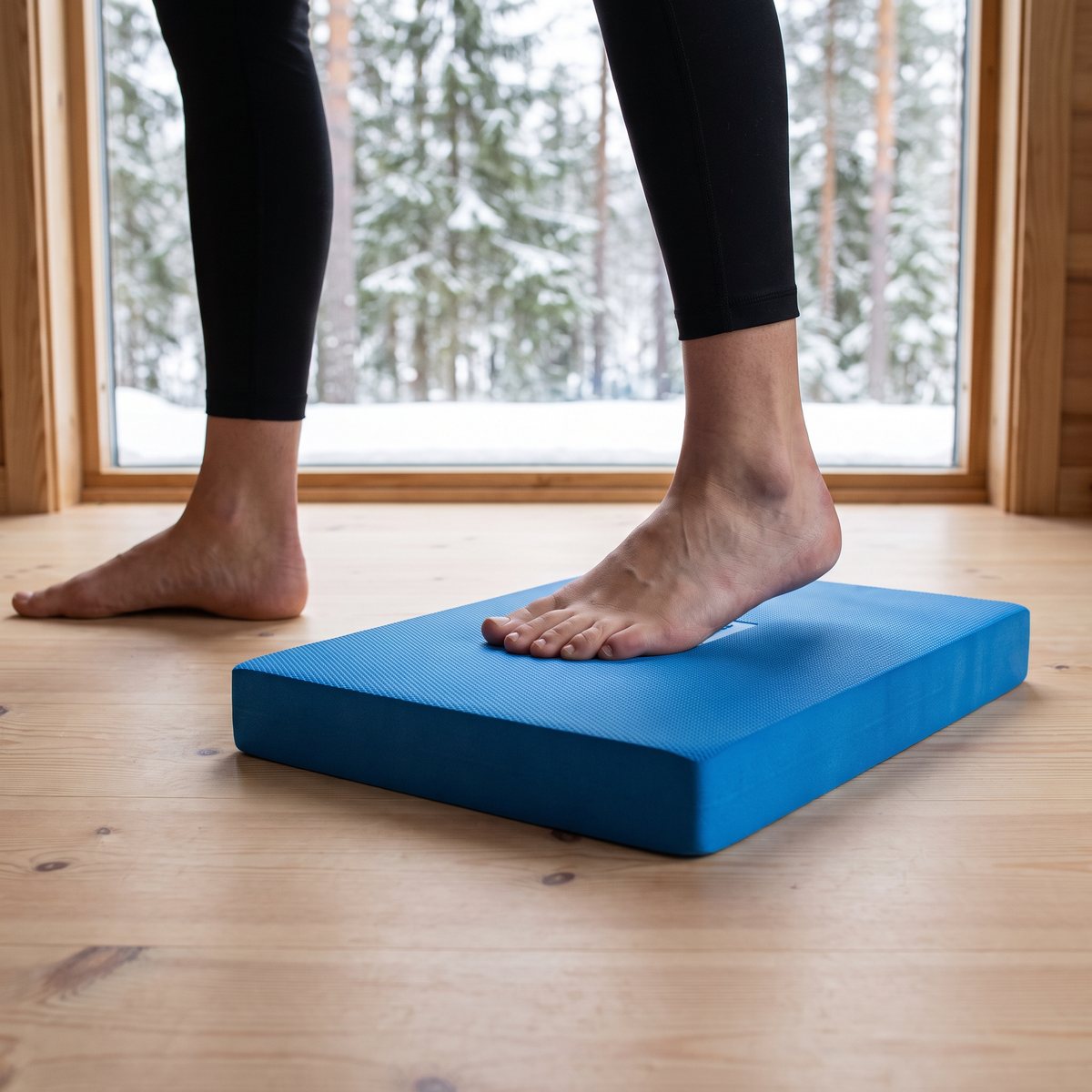Gorilla Sports balansplatta i skum, med fötter i en svensk stuga med snöig granskog utanför fönstret.