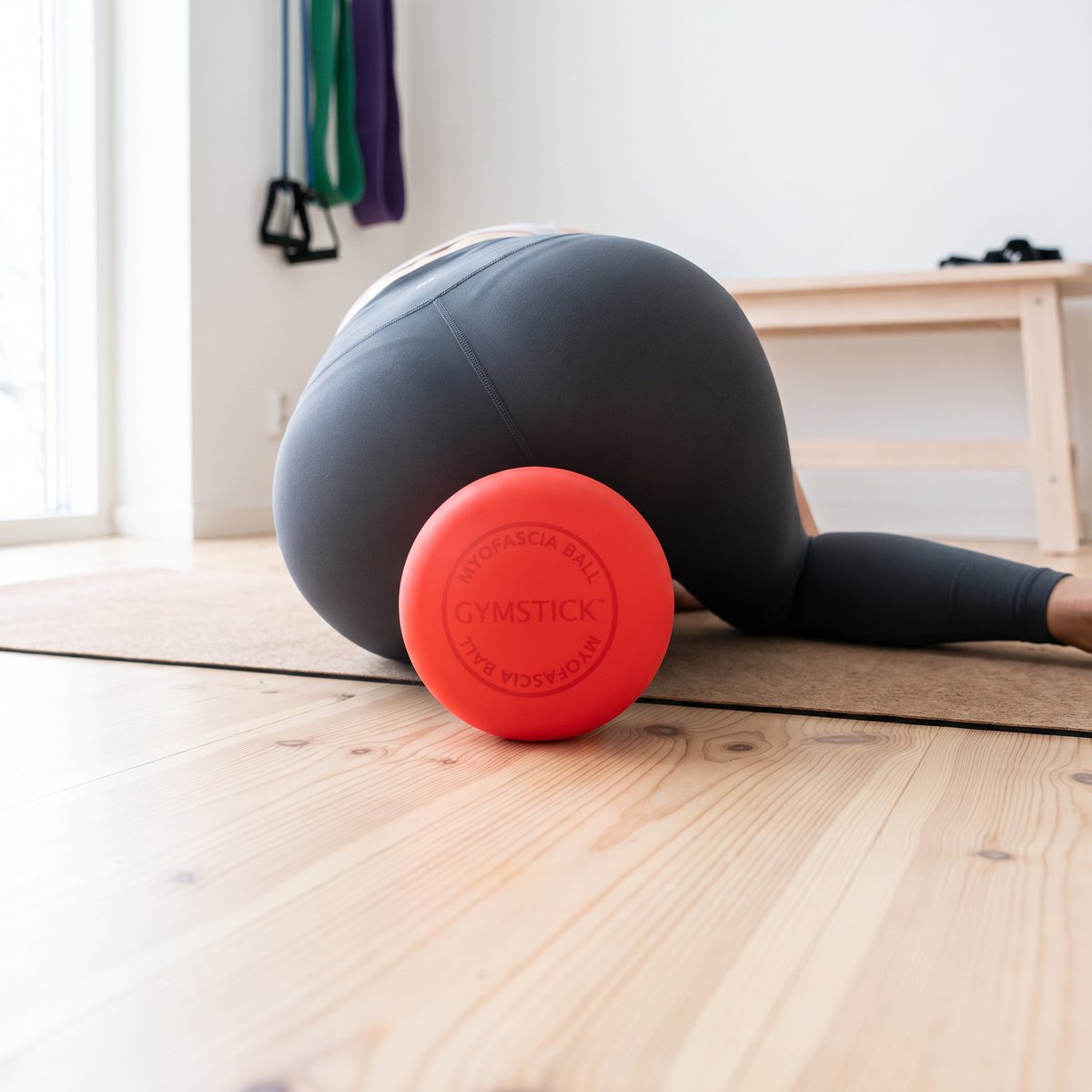 Röd massageboll från Gymstick mellan höften och ett trägolv vid självmassage i ett svenskt hemmagym