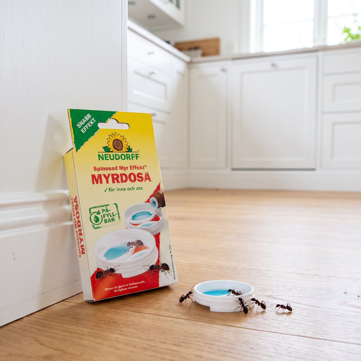 Neudorff Myr Effekt myrdosa lutad mot en list på trägolvet i ett ljust svenskt kök, med en dosa som myror närmar sig