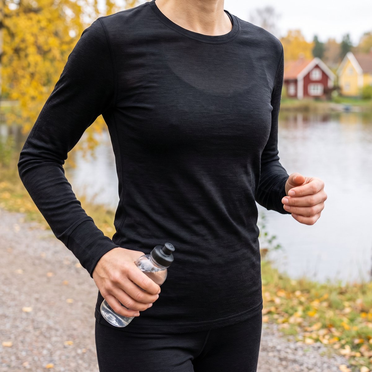 Kvinna joggar i tunn svart Supernatural-tröja med rund hals längs en sjö i en svensk småstad på hösten